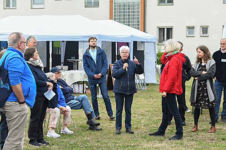 Seniorin mit Mikrofon in der Hand, darum hören Menschen ihr zu