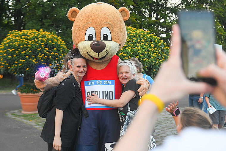 Ein großes Bären-Maskottchen posiert für eine Foto mit den Besuchern eines Parks.